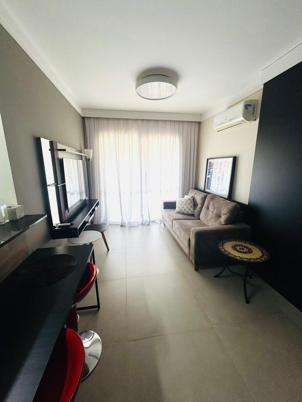 Sala de estar com sofá, TV e cortinas para a varanda